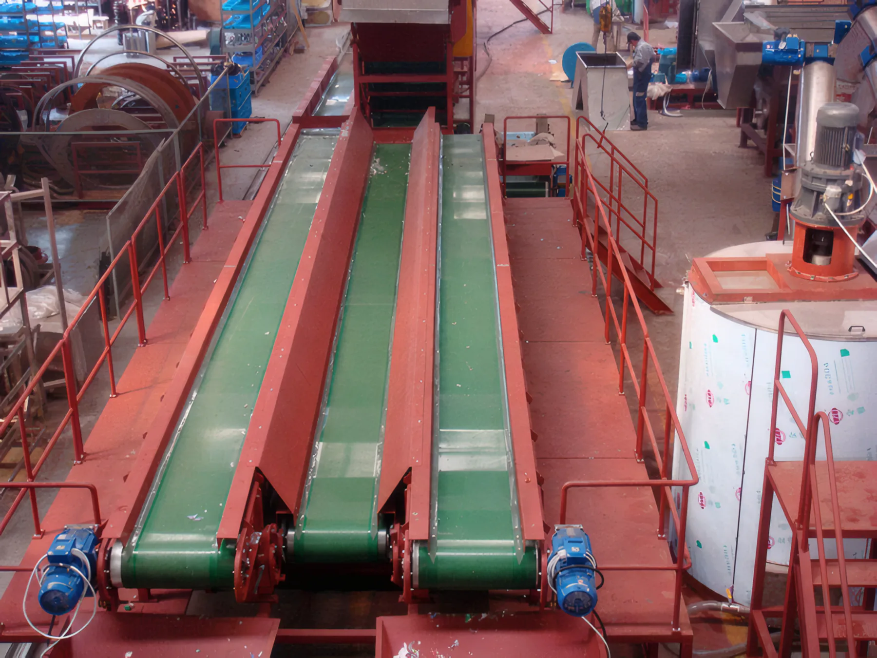 Twin green sorting conveyors beside a stainless tank